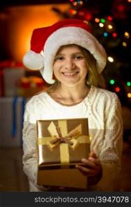 Portrait of happy laughing girl in Santa cap holding golden gift box