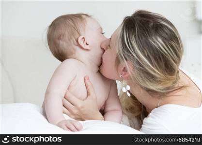 Portrait of happy laughing mother kissing her baby boy on bed