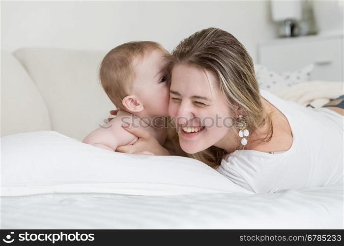 Portrait of happy laughing mother playing with her baby boy on bed