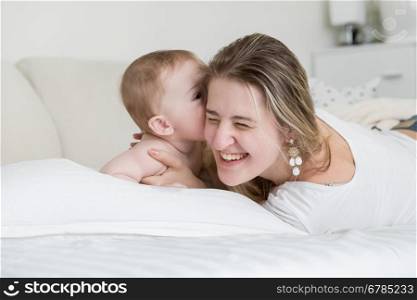 Portrait of happy laughing mother playing with her baby boy on bed