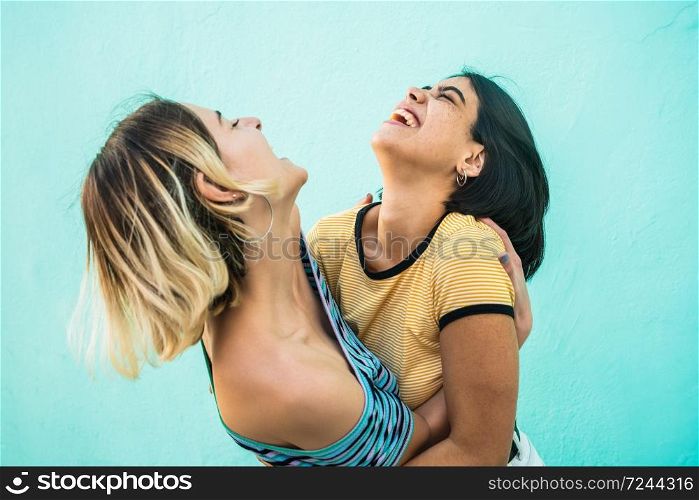 Portrait of happy lesbian couple having fun and hugging against light blue background. LGBT concept.