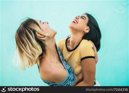 Portrait of happy lesbian couple having fun and hugging against light blue background. LGBT concept.