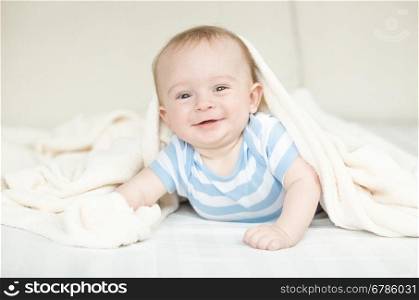 Portrait of happy little baby crawling on bed under blanket