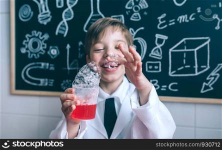 Portrait of happy little boy holding glass with soap foam against of blackboard with drawings. Happy hid holding glass with soap foam