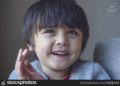 Portrait of happy little boy looking at camera with smiling face, Head shot Healthy child sitting on sofa, Positive kid relaxing at home on weekend during Autumn or winter time