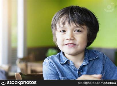 Portrait of happy little boy with smile sitting in the cafe waitting for food, Cheerful kid looking at camera with smling face, Positive childhood concept