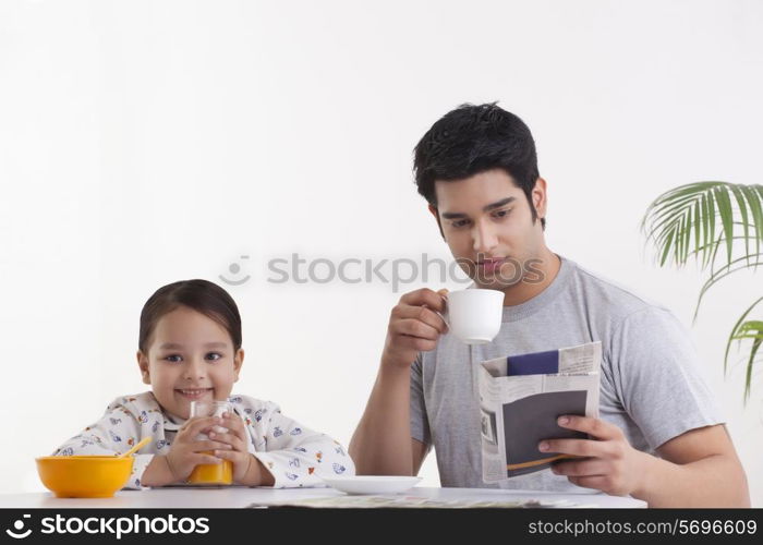 Portrait of happy little girl drinking juice while father reading newspaper