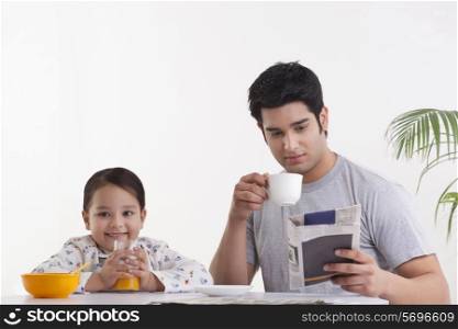 Portrait of happy little girl drinking juice while father reading newspaper