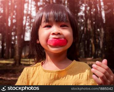 Portrait of happy little girl eating red apple outdoors in summer. Childhood happiness.