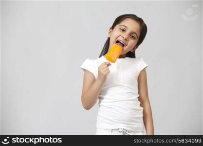 Portrait of happy little girl licking ice lolly isolated over gray background