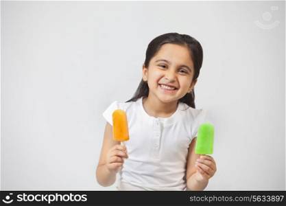 Portrait of happy little girl with ice lollies isolated over gray background