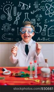 Portrait of happy little scientist with glasses laughing behind of red table with experiment elements. Happy kid with glasses laughing behind of experiments table