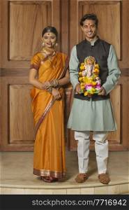 Portrait of happy maharashtrian couple in traditional dress celebrating ganapati festival holding a small statue of lord ganesha.