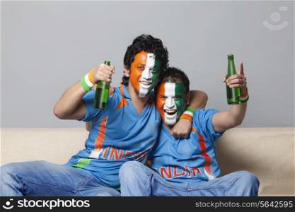 Portrait of happy male friends with face painted in tricolor enjoying drink together at home