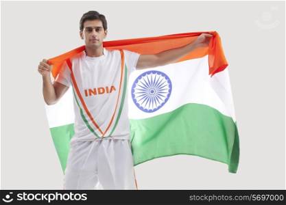 Portrait of happy male hockey player celebrating victory with Indian flag against gray background