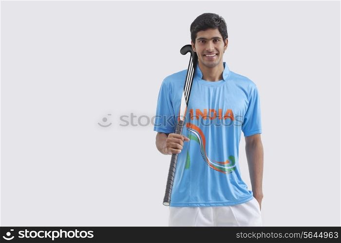 Portrait of happy male hockey player with stick standing against white background