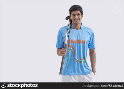 Portrait of happy male hockey player with stick standing against white background