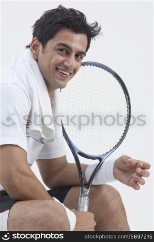 Portrait of happy male tennis player holding racket isolated over gray background