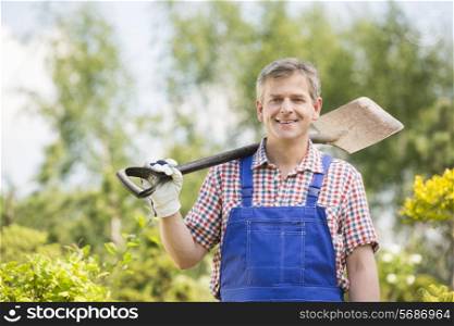 Portrait of happy man carrying spade on shoulder in plant nursery