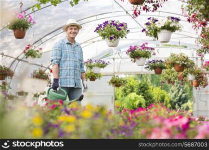 Portrait of happy man carrying watering can in greenhouse