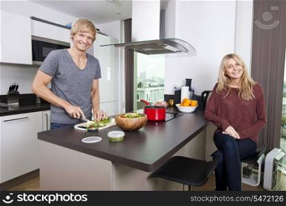 Portrait of happy man cutting vegetables while woman sitting at kitchen counter