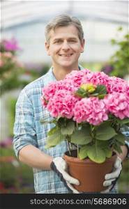 Portrait of happy man holding flower pot in greenhouse