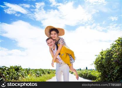 Portrait of happy man piggybacking woman on footpath amidst field against cloudy sky