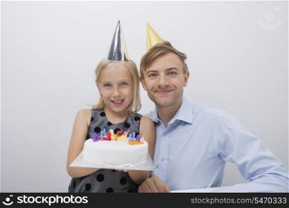 Portrait of happy man with daughter holding birthday cake against gray background