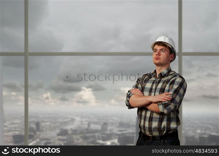Portrait of happy mature architect in helmet standing with arms crossed on chest. Confident builder man