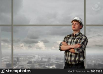Portrait of happy mature architect in helmet standing with arms crossed on chest. Confident builder man