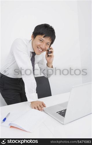 Portrait of happy mid adult businessman using cell phone at desk