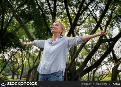Portrait of happy middle aged woman dancing in the park. The woman is smiling with happiness. Retirement concept.. Happy middle aged woman standing in the park.