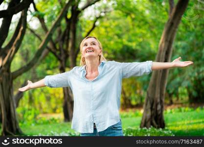 Portrait of happy middle aged woman dancing in the park. The woman is smiling with happiness. Retirement concept.