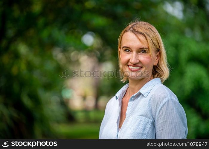 Portrait of happy middle aged woman standing in the park. The woman is smiling with happiness.