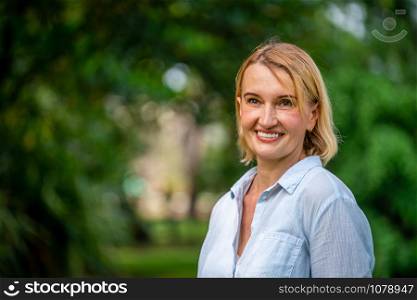 Portrait of happy middle aged woman standing in the park. The woman is smiling with happiness.