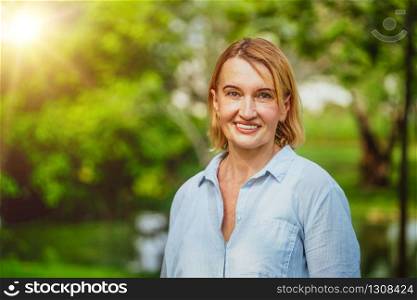 Portrait of happy middle aged woman standing in the park. The woman is smiling with happiness.. Happy middle aged woman standing in the park.