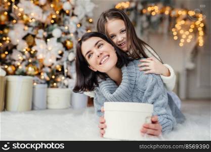 Portrait of happy mother and daughter spend free time together, embrace each other, have pleasant smiles, hold wrapped present boxes, celebrate New Year or Christmas together. Holidays concept