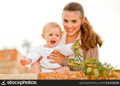 Portrait of happy mother and laughing baby playing with plants &#xA;