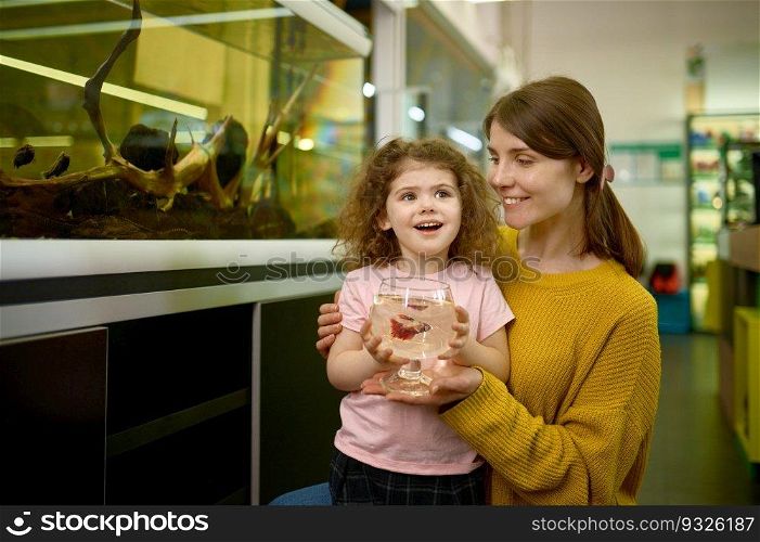 Portrait of happy mother and little daughter bought fish at pet shop. Focus on amazed kid face. Portrait of happy mother and little daughter bought fish at pet shop