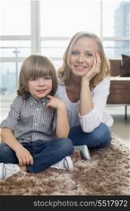 Portrait of happy mother sitting with boy on rug in living room