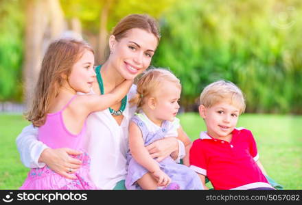 Portrait of happy mother with cute little babies sitting on fresh green grass field, having fun outdoors, enjoying parenthood, happiness and love concept