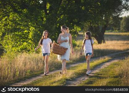 Portrait of happy mother with two daughter walking by the river in meadow