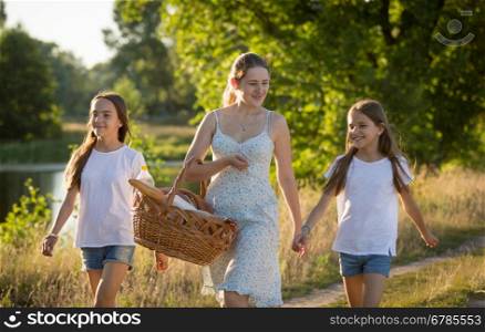 Portrait of happy mother with two daughter walking by the river in meadow at sunset