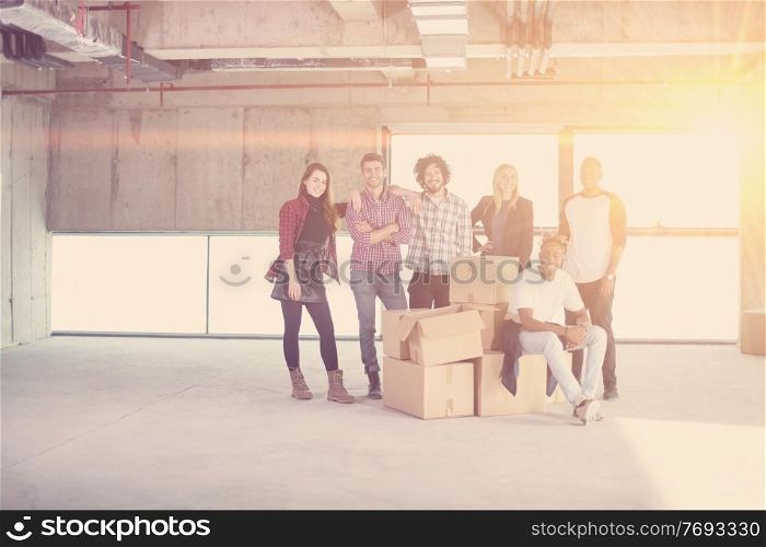 portrait of happy multiethnic business team with sunlight through the windows and cardboard boxes around them during movin in at new unfinished startup office building