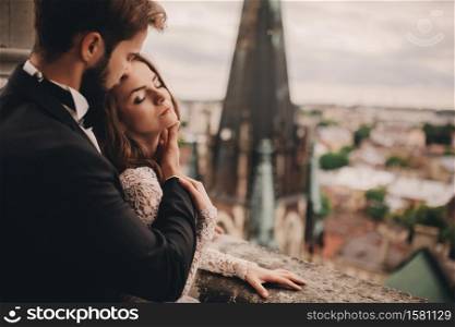 portrait of Happy newlywed. beautiful bride and stylish groom are hugging on the balcony of old gothic cathedral with panoramic city views.. portrait of Happy newlywed. beautiful bride and stylish groom are hugging on the balcony of old gothic cathedral with panoramic city views