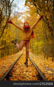 Portrait of happy overjoyed woman in jump over railroad in autumn forest. Excitement and fall weather. Woman jumping over railroad in autumn forest