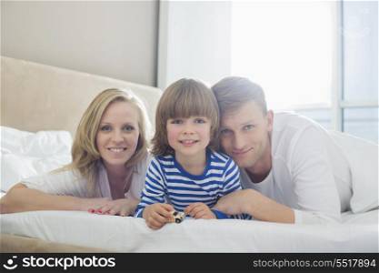 Portrait of happy parents lying with son in bed
