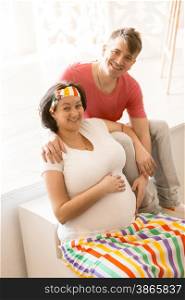 Portrait of happy pregnant couple hugging and looking at camera