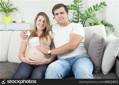 Portrait of happy pregnant couple sitting on sofa and looking at each other