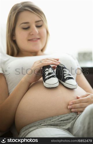 Portrait of happy pregnant woman lying on sofa and holding baby boots